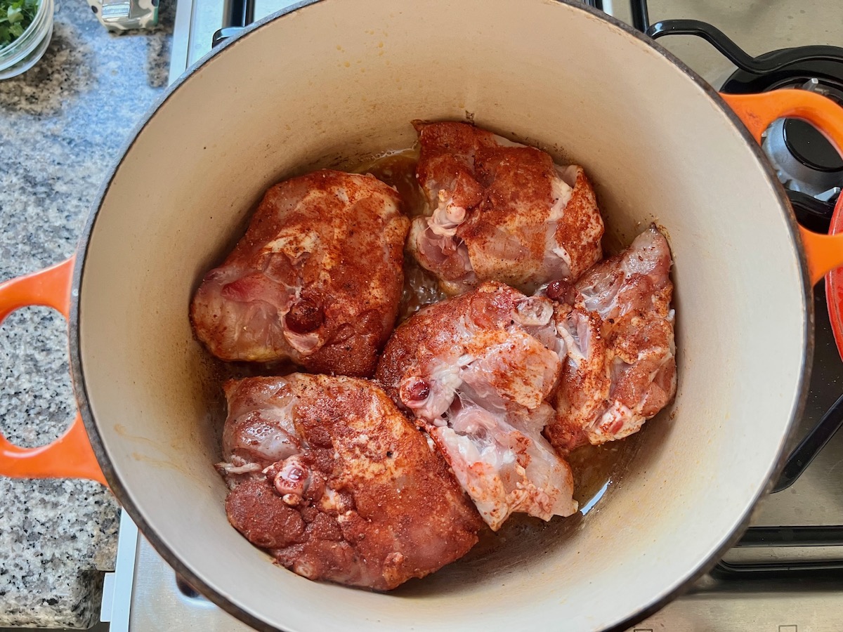 Seasoned chicken thighs with bone in a dutch oven pot for Spanish Chicken Soup Recipe.