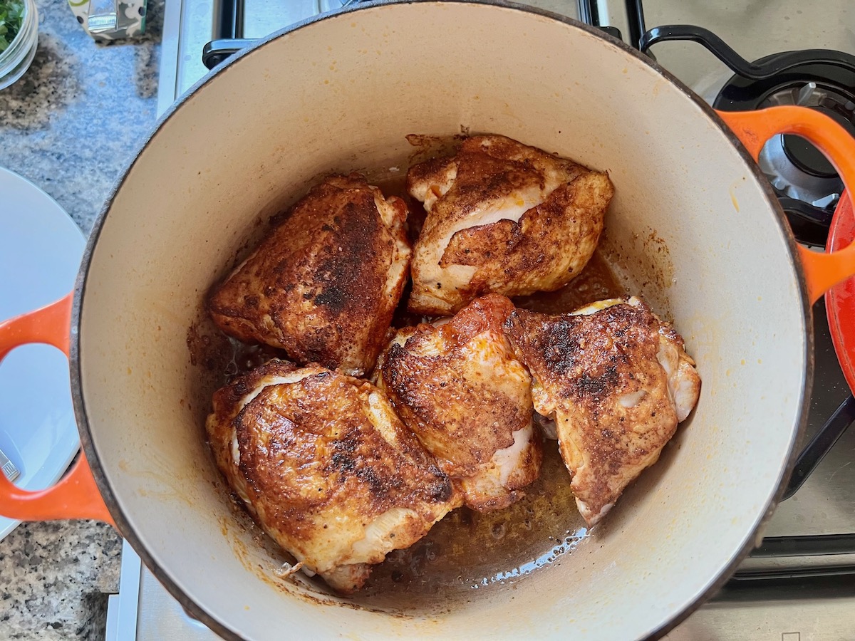 Seared seasoned chicken thighs with bone in a dutch oven pot for Spanish Chicken Soup Recipe.