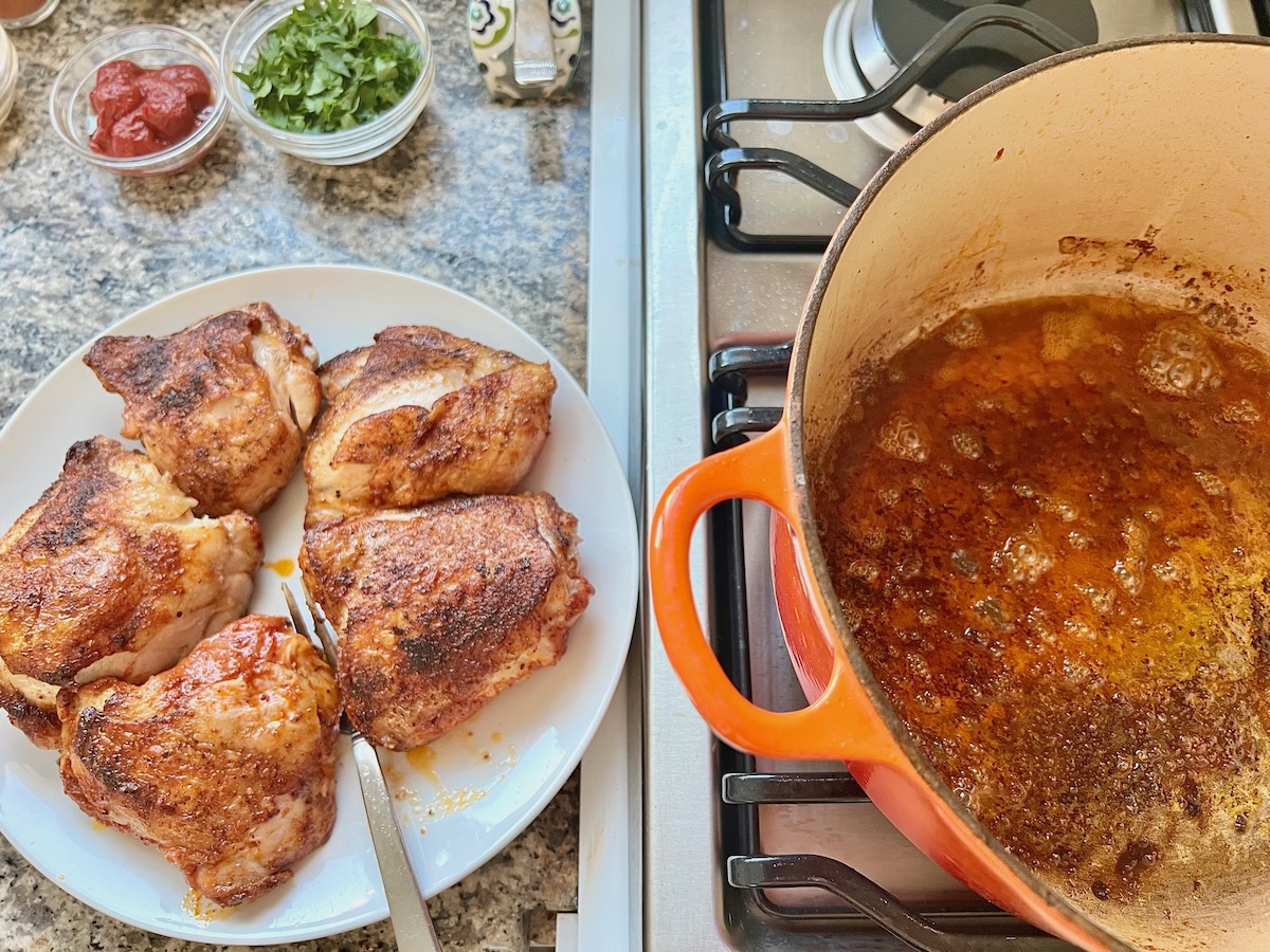 Seasoned and seared chicken thighs transferred to a plate from a dutch oven pot for Spanish Chicken Soup Recipe.