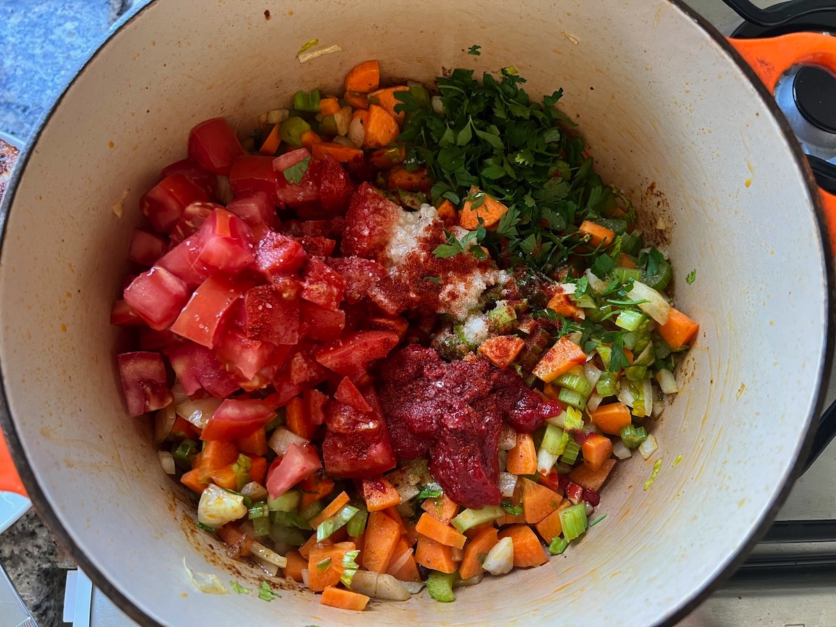 Tomatoes, tomato paste, parsley, and seasoning add to carrots, onions, celery, in pot for Spanish Chicken Soup Recipe.