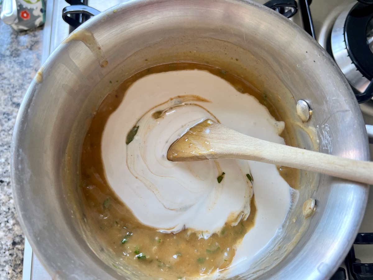 Sour cream bring mixed into the enchilada sauce in a pot with a wood spoon for crockpot white chicken enchilada casserole.
