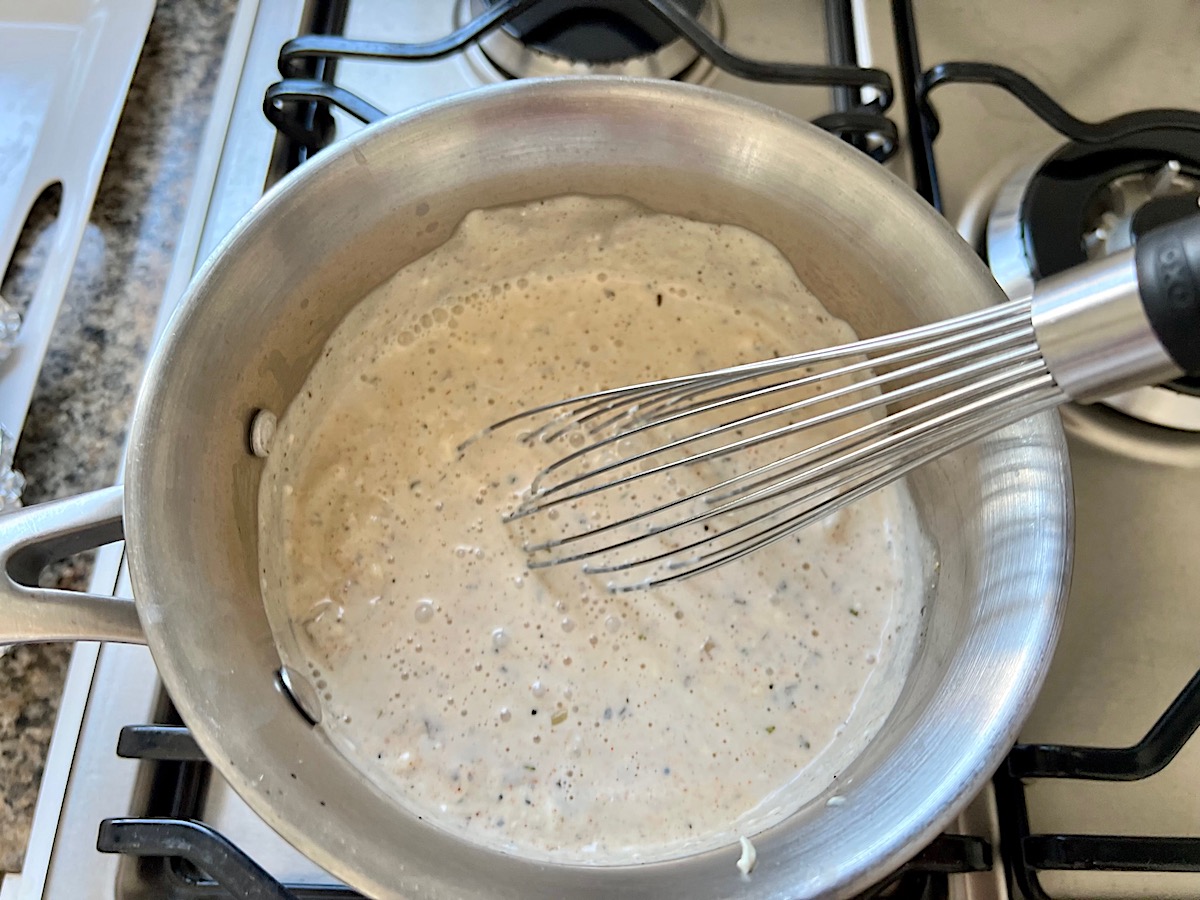 Whisking the cream cheese, broth, and slurry into the sauce for the Low Carb Cauliflower Rice Chicken Casserole.