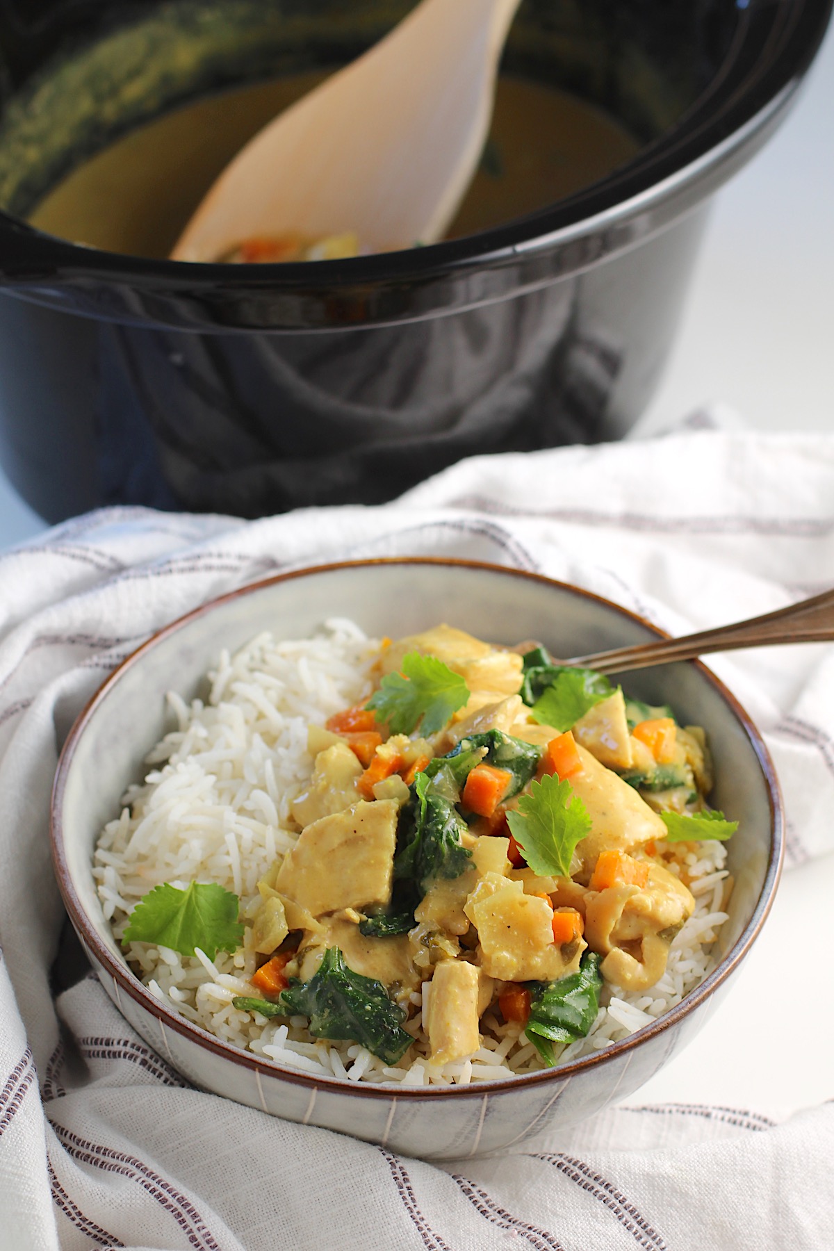 Crockpot Thai Chicken Curry over rice in a bowl with fork and slow cooker in background with spoon.