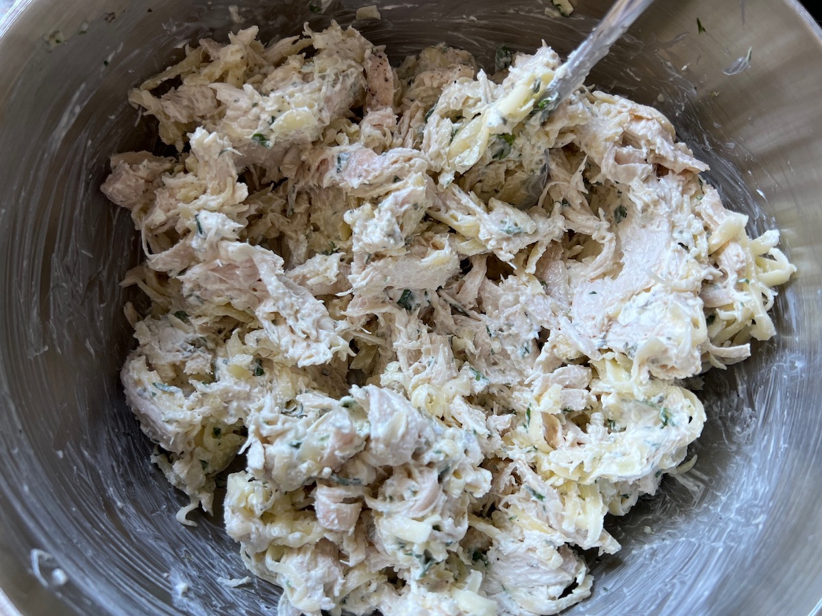 Mixed shredded mozzarella, cooked shredded chicken, softened cream cheese, parsley, garlic, oregano, salt, and pepper in a metal bowl for Broccoli and Chicken Lasagna recipe.