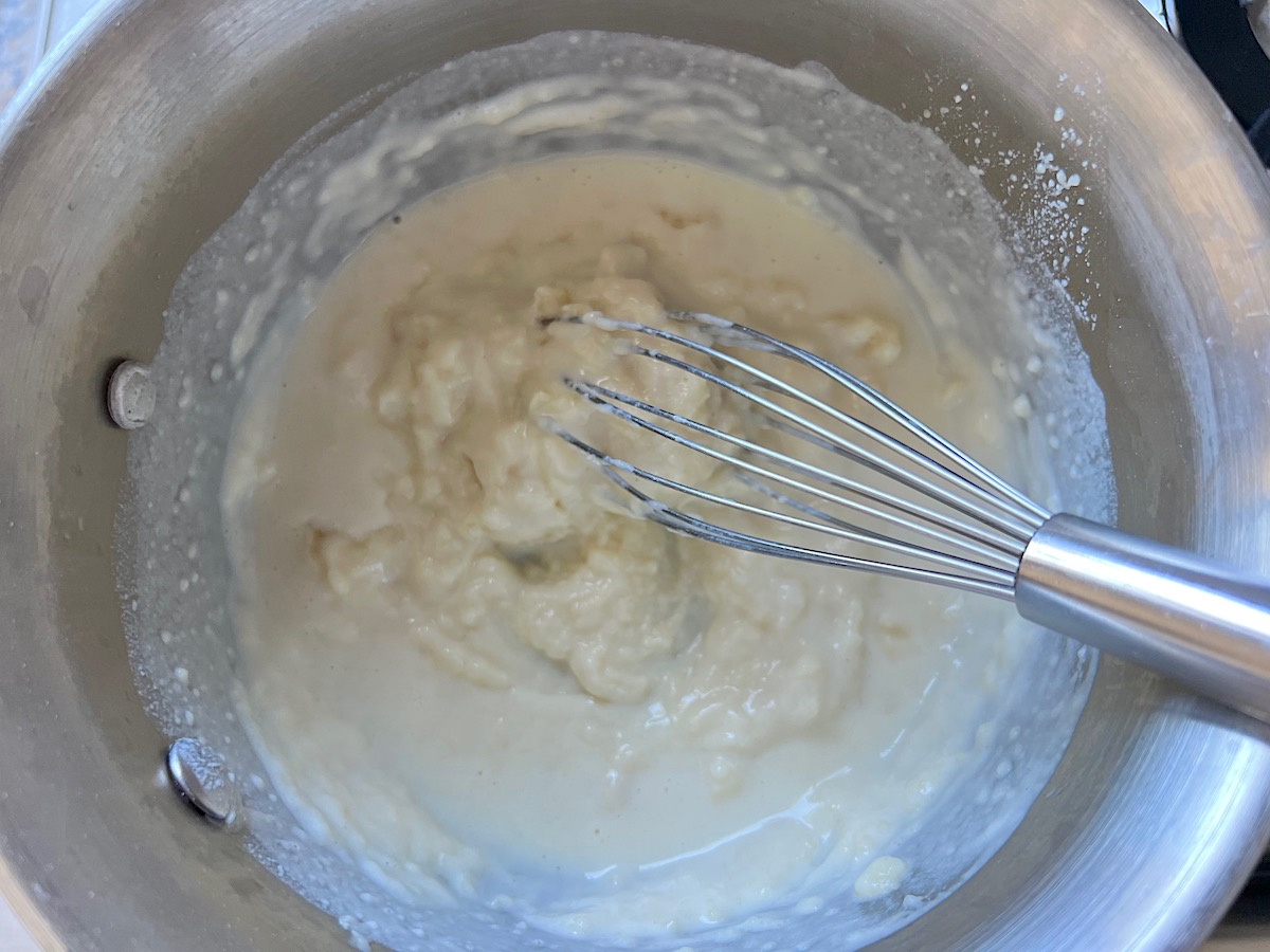 Whisk in a saucepan mixing milk into the flour and butter roux for Broccoli and Chicken Lasagna recipe.