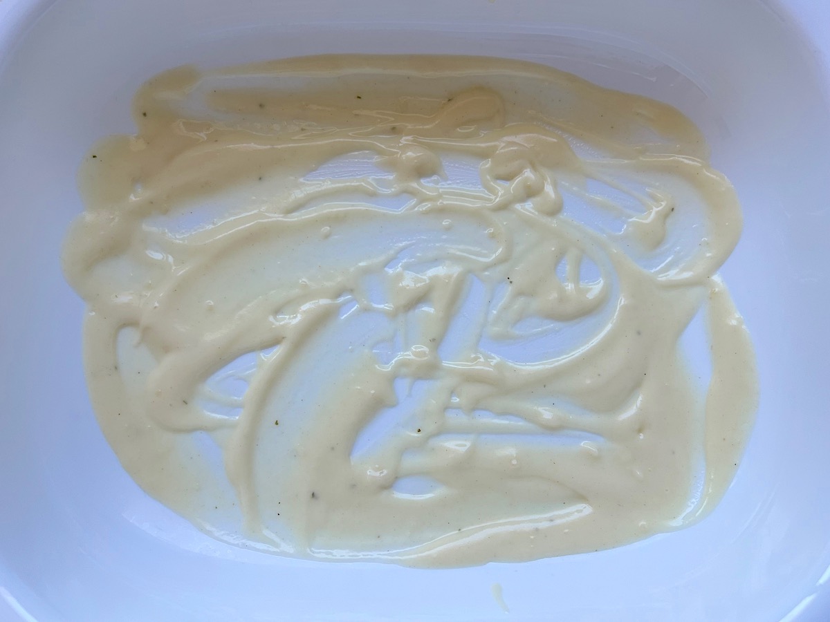 LBechamel sauce spread on the bottom of a casserole dish for Broccoli and Chicken Lasagna Recipe.