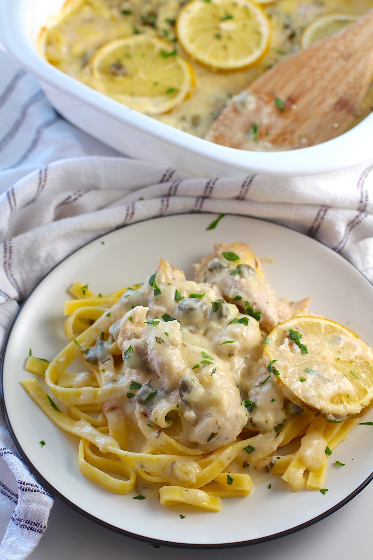 Creamy Chicken Piccata Casserole Recipe served on a plate over pasta with the casserole dish in the background.