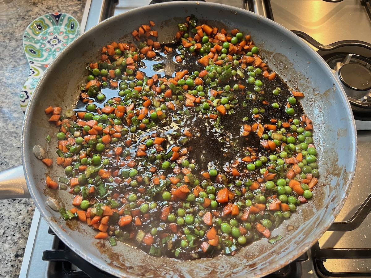 Diced carrots scallions, and soy sauce cooking in a frying pan for Shrimp and Chicken Fried Rice recipe.