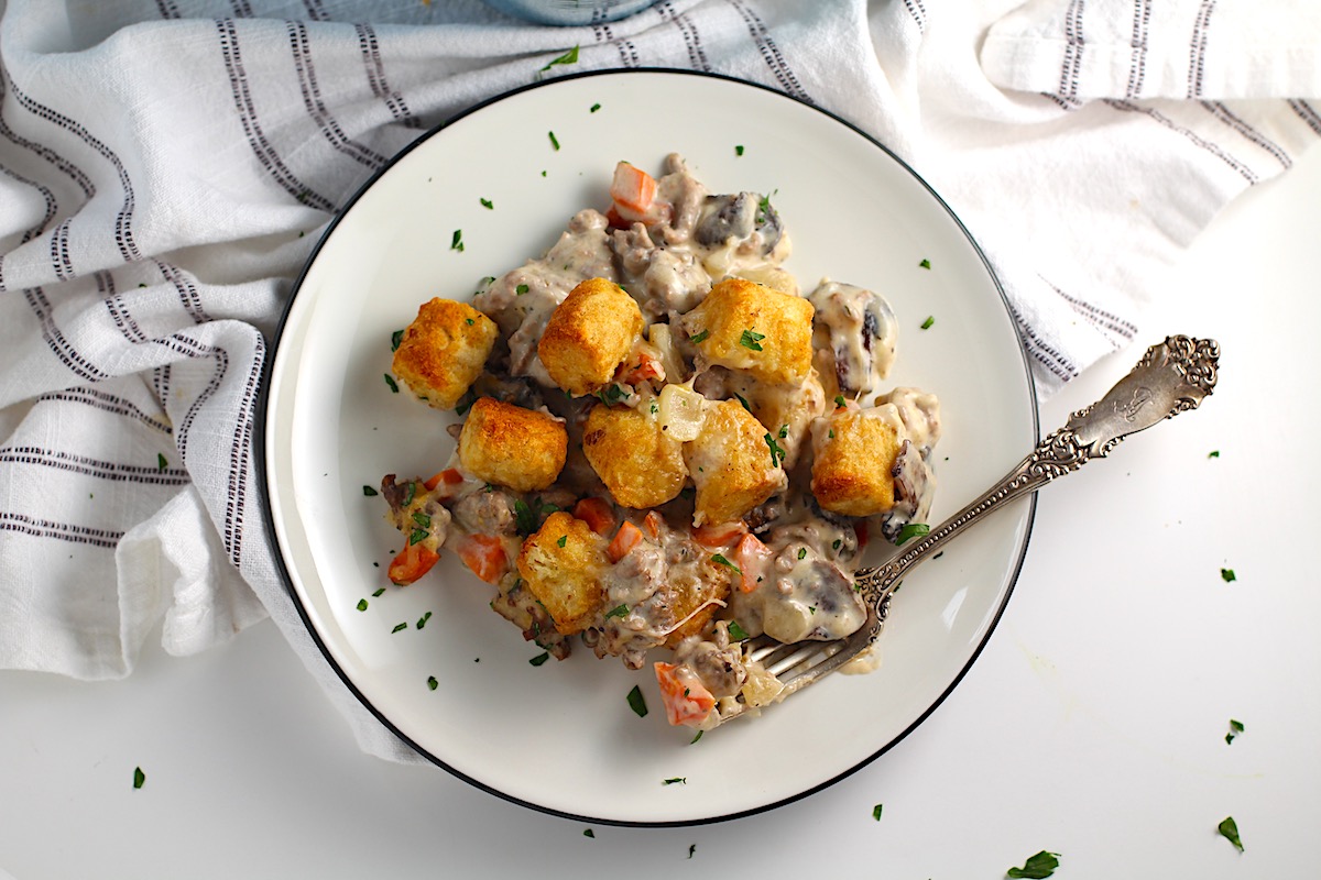 Creamy and cheesy hamburger tater tot casserole recipe on a plate with a fork and parsley sprinkled on top.