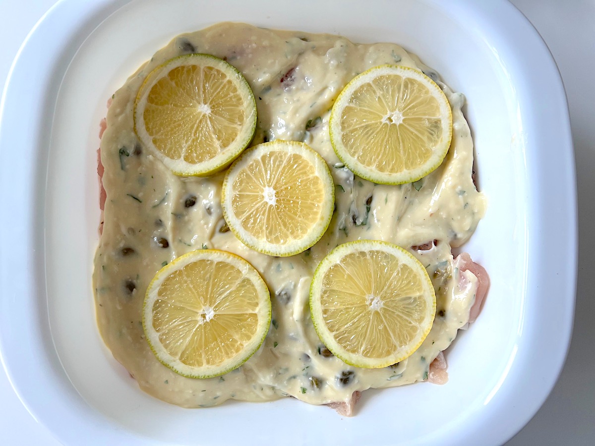 Creamy Piccata sauce poured over chicken in casserole dish then topped with lemon slices for the Creamy Chicken Piccata Casserole recipe.for the Creamy Chicken Piccata Casserole recipe.