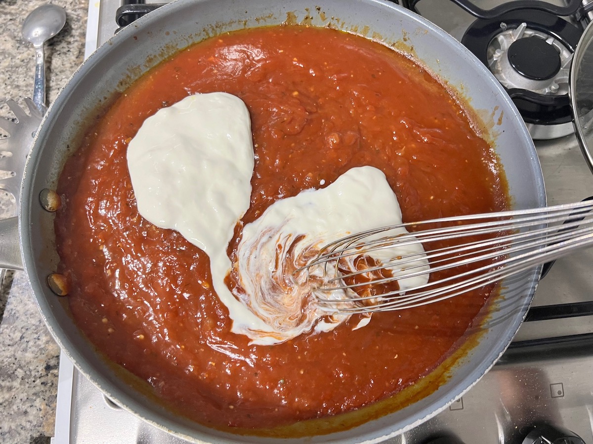 Whisk mixing heavy cream into tomato sauce for Chicken and Vodka pasta sauce recipe.