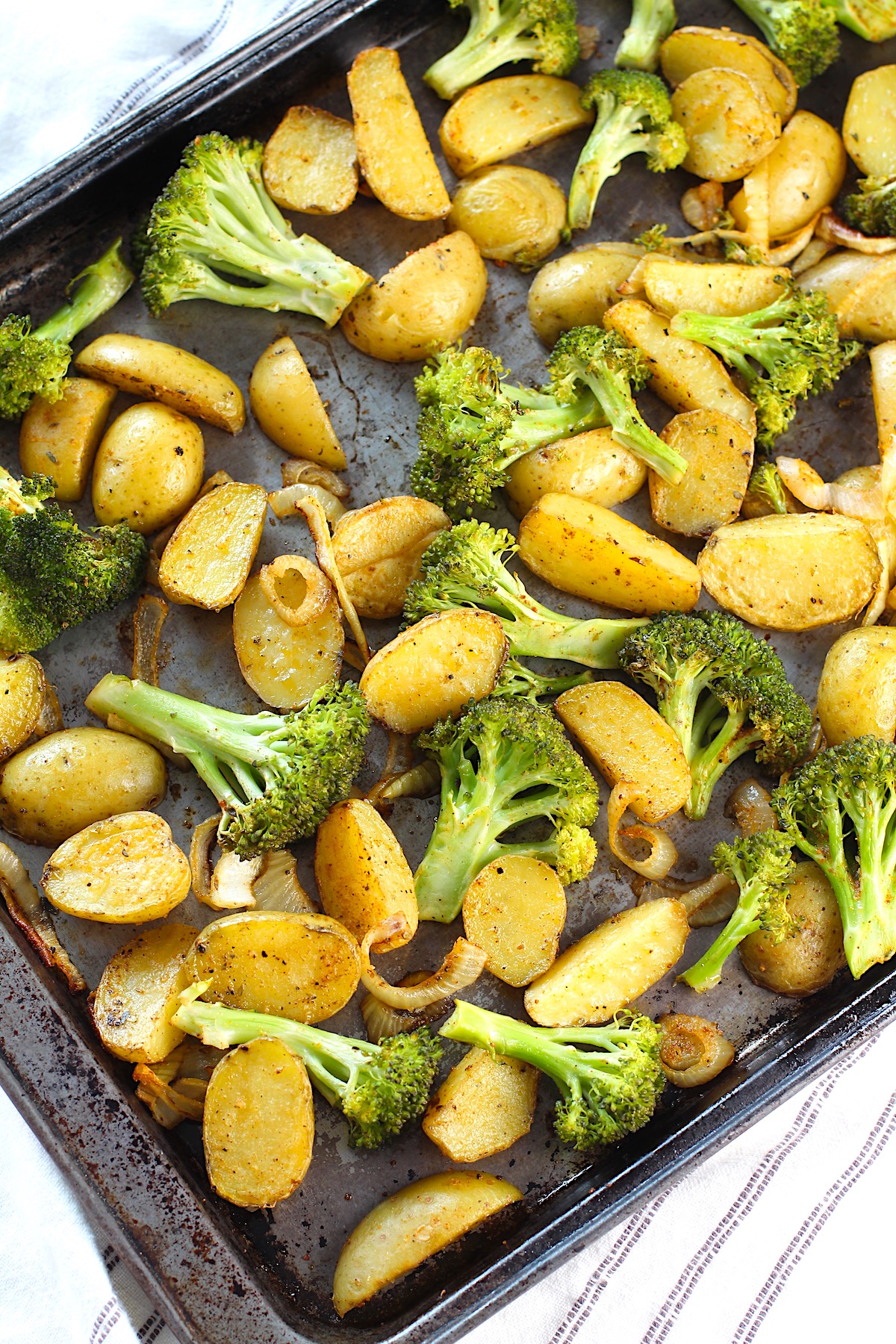 Roasting Potatoes and Broccoli with onions on a sheet pan.  The potatoes are cut, golden brown, and crispy.  The broccoli is toasty and tender.