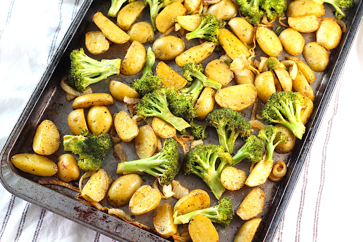 Roasting Potatoes and Broccoli with onions on a sheet pan. The potatoes are cut, golden brown, and crispy. The broccoli is toasty and tender.