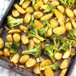 Roasting Potatoes and Broccoli with onions on a sheet pan. The potatoes are cut, golden brown, and crispy. The broccoli is toasty and tender.