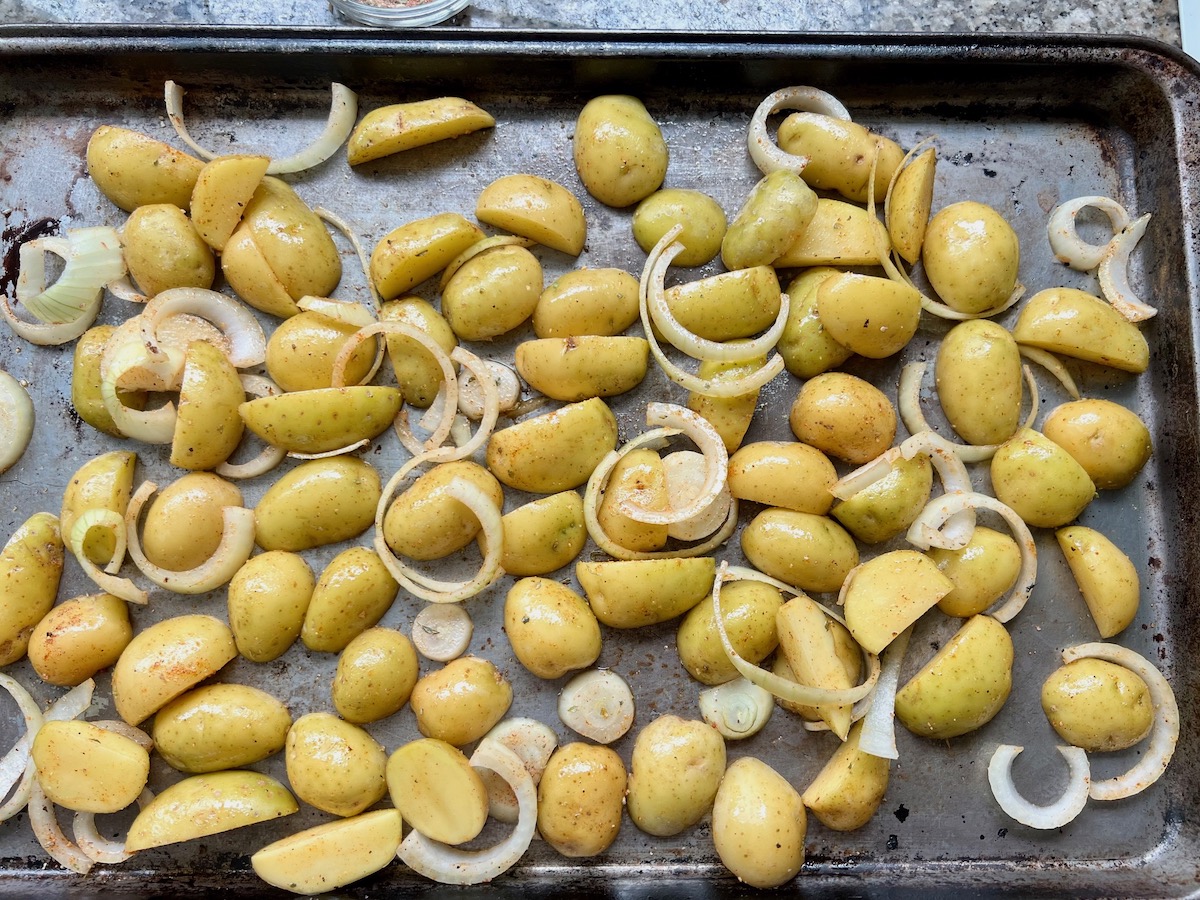 Potatoes and onion slices spread out on a sheet pan for Roasting Potatoes and Broccoli recipe.