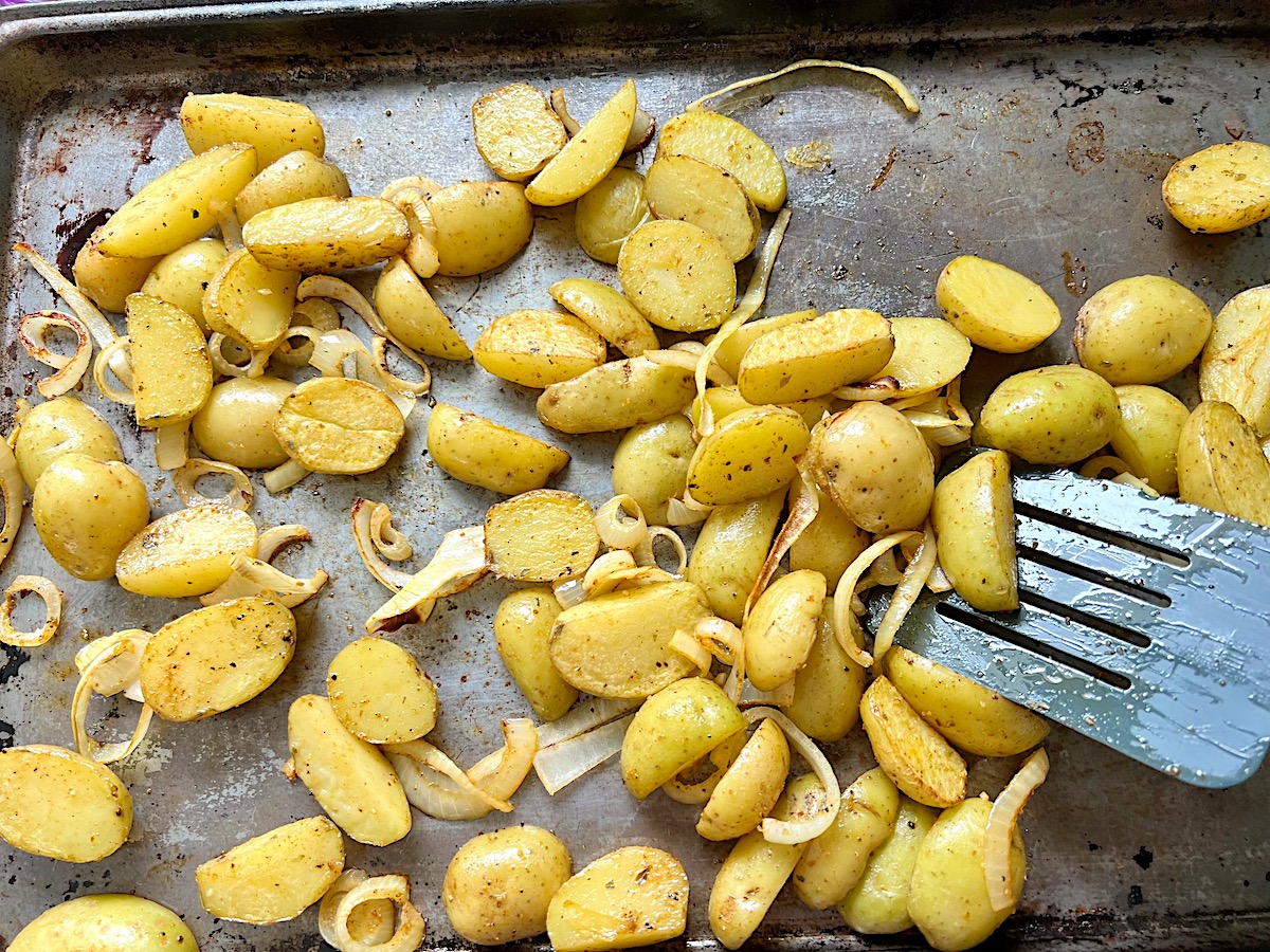 Spatula tossing the potatoes and onion slices on a sheet pan for Roasting Potatoes and Broccoli recipe.