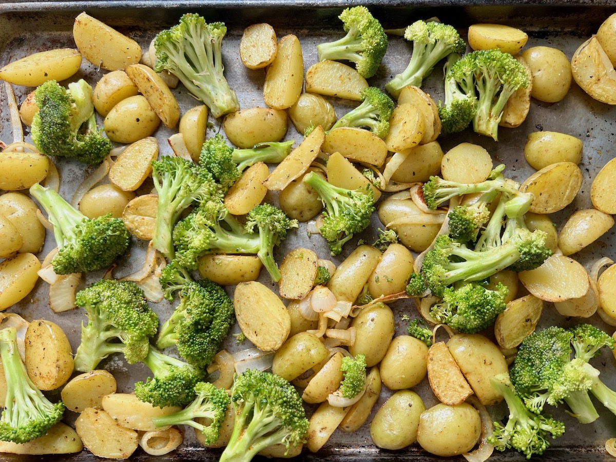 Seasoned raw broccoli added to the pan of potatoes and onions that have already been roasting.