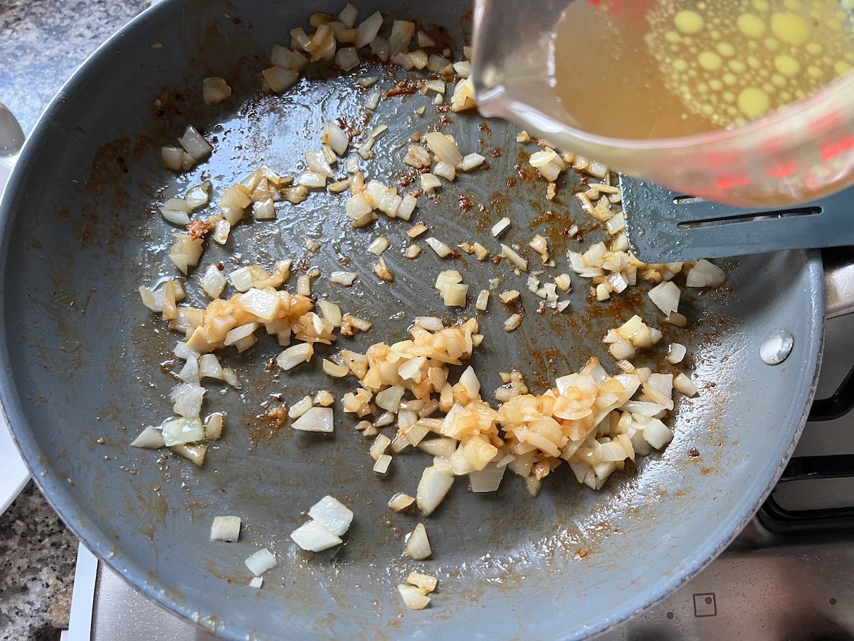 Chicken broth being combined in the skillet with the onion and garlic.