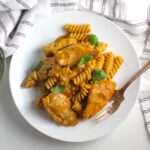 A serving of butter chicken pasta on a plate with a fork on the edge.