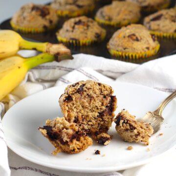 An oat banana chocolate chip muffin on a plate with pieces of the muffin cut away and one on a fork, that shows the melted chocolate.