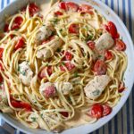 Boursin Tomato Pasta with chicken, fettuccine noodles, and cherry tomatoes in a killet on table with blue and white tablecloth.