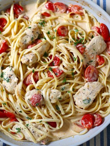Boursin Tomato Pasta with chicken, fettuccine noodles, and cherry tomatoes in a killet on table with blue and white tablecloth.