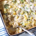 Chicken Broccoli Potato Casserole with fresh oregano on top in a casserole dish with a serving spoon scooping in the corner.