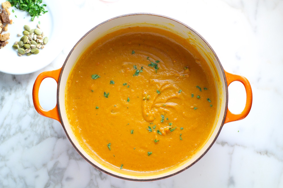 Creamy Carrot and Lentil Soup blended smooth in a pot on counter garnished with parsley.