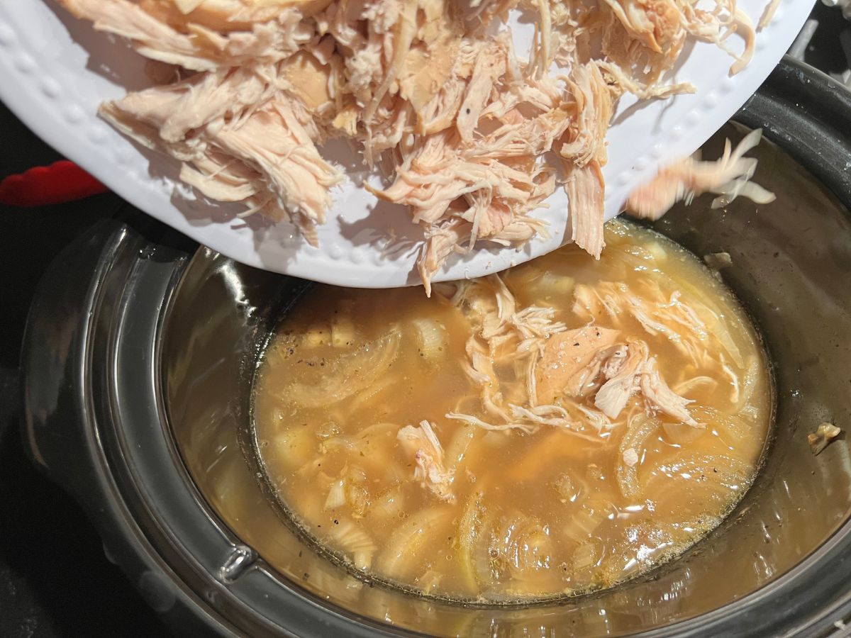 Shredded chicken being added back to the soup mixture in the crockpot.