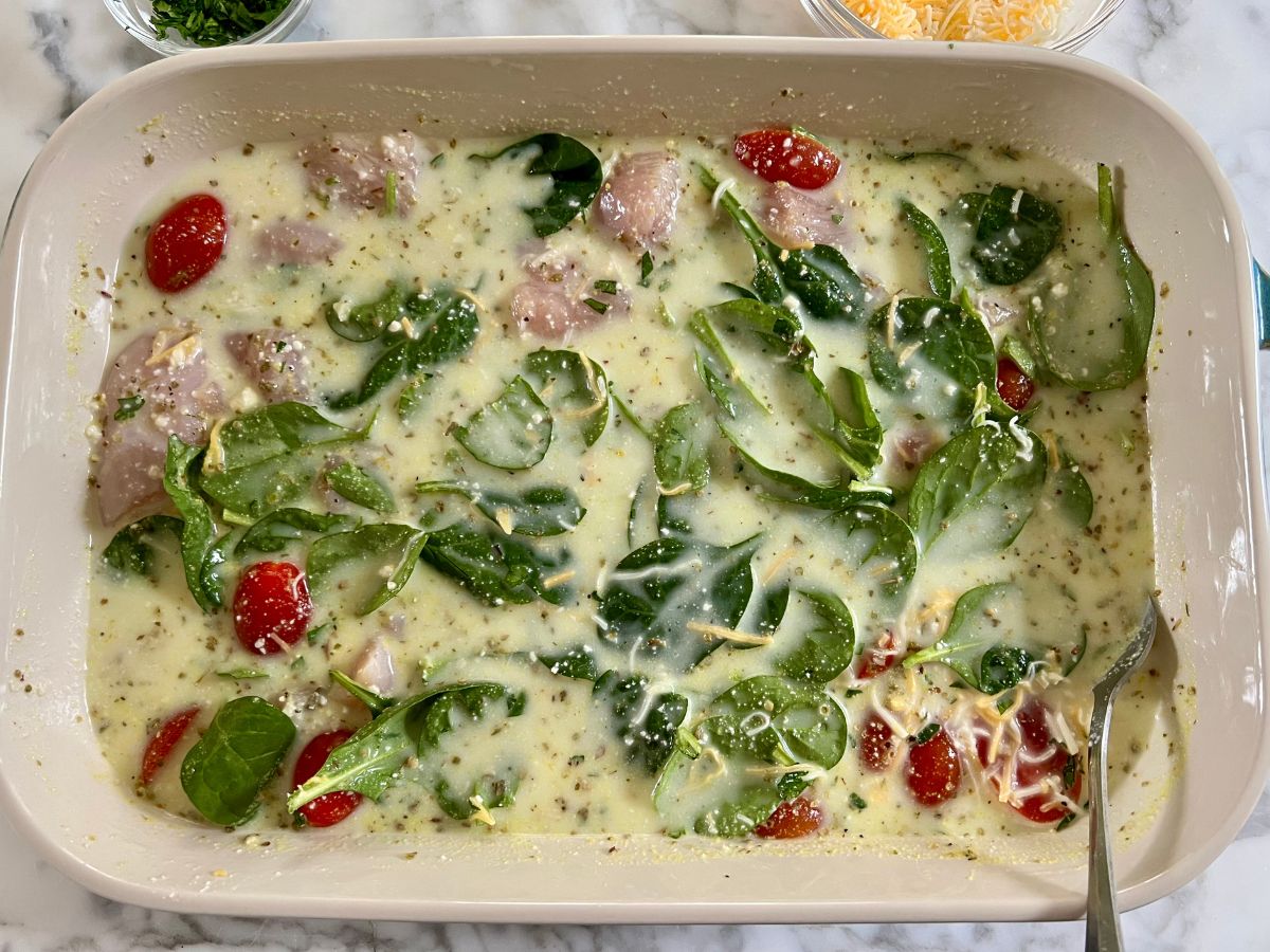 Spoon resting in a mixture of spinach, tomatoes, chicken pieces and cheese within the broth mixture.