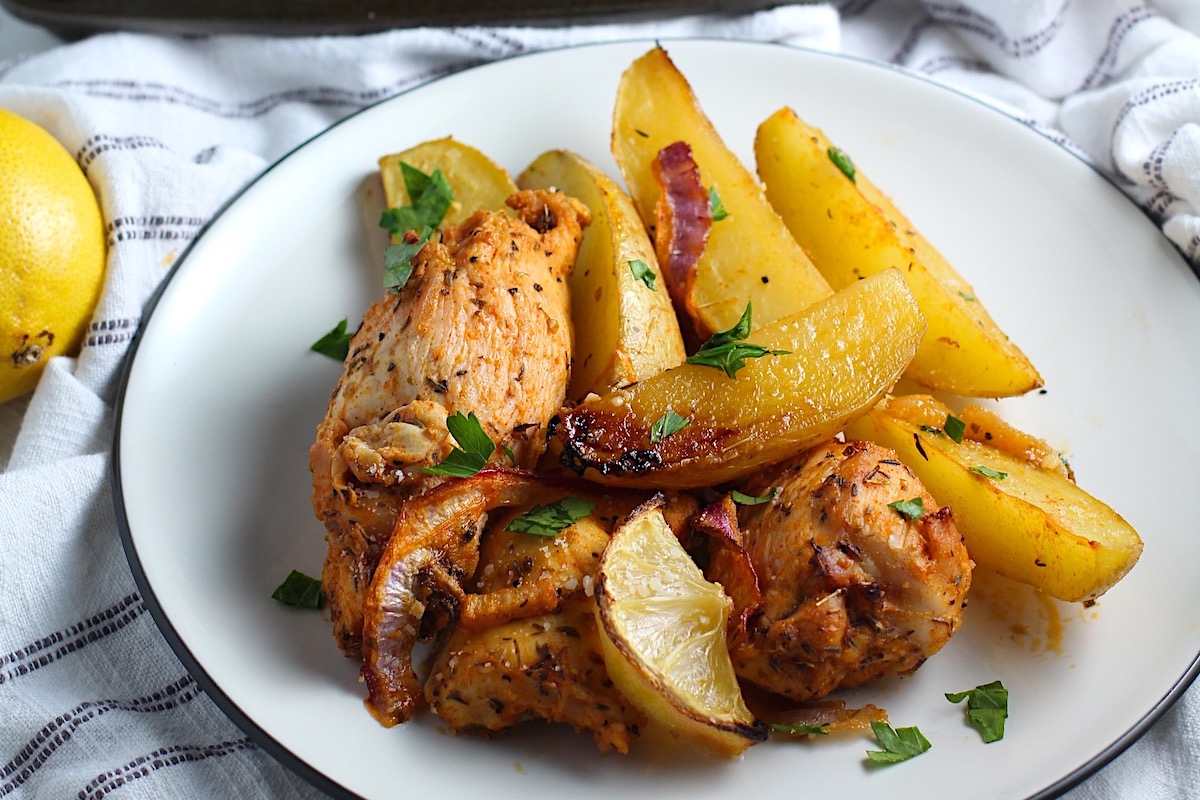 Crispy, golden brown Greek Lemon Chicken and Potatoes with red onions and fresh parsley garnish on a plate.
