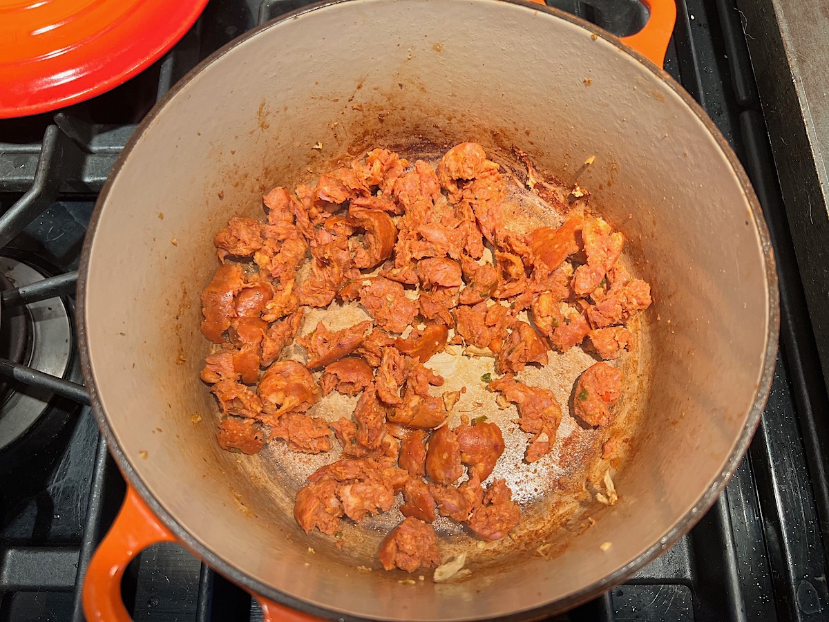 Cooked Chorizo broken up and rendering in a pot on stove for Chicken Chorizo Orzo.