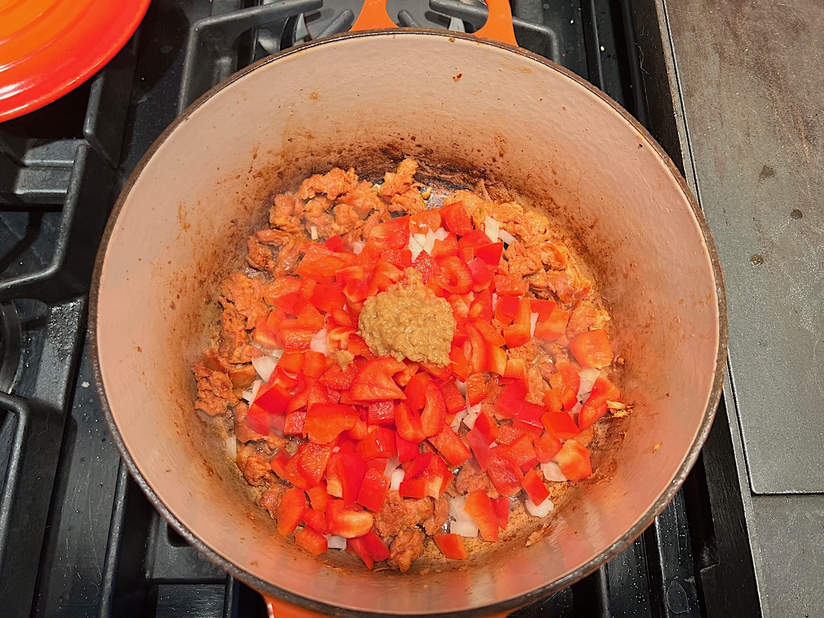 Chorizo, red pepper, onion, and garlic cooking in a pot on stove for Chicken Chorizo Orzo.