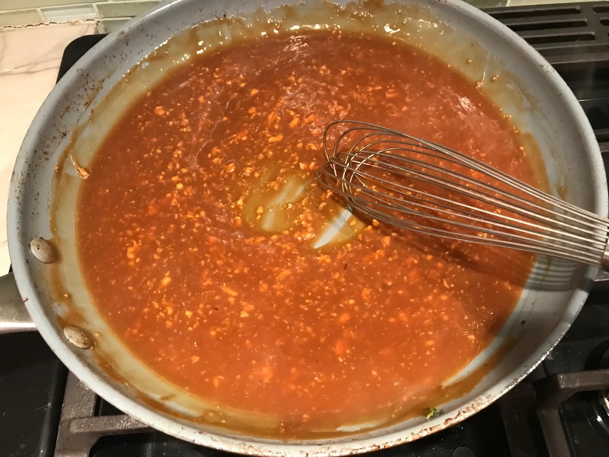 Sauce added to pan and starting to thicken with a whisk leaving a track in the pan for Beef and Broccoli Noodles recipe.