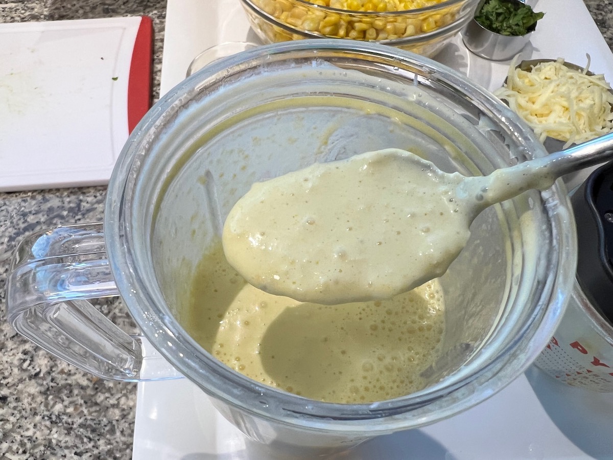 Spoon in blender to look at consistency of blended broth, cream cheese, and corn for the Mexican Street Corn Casserole recipe.