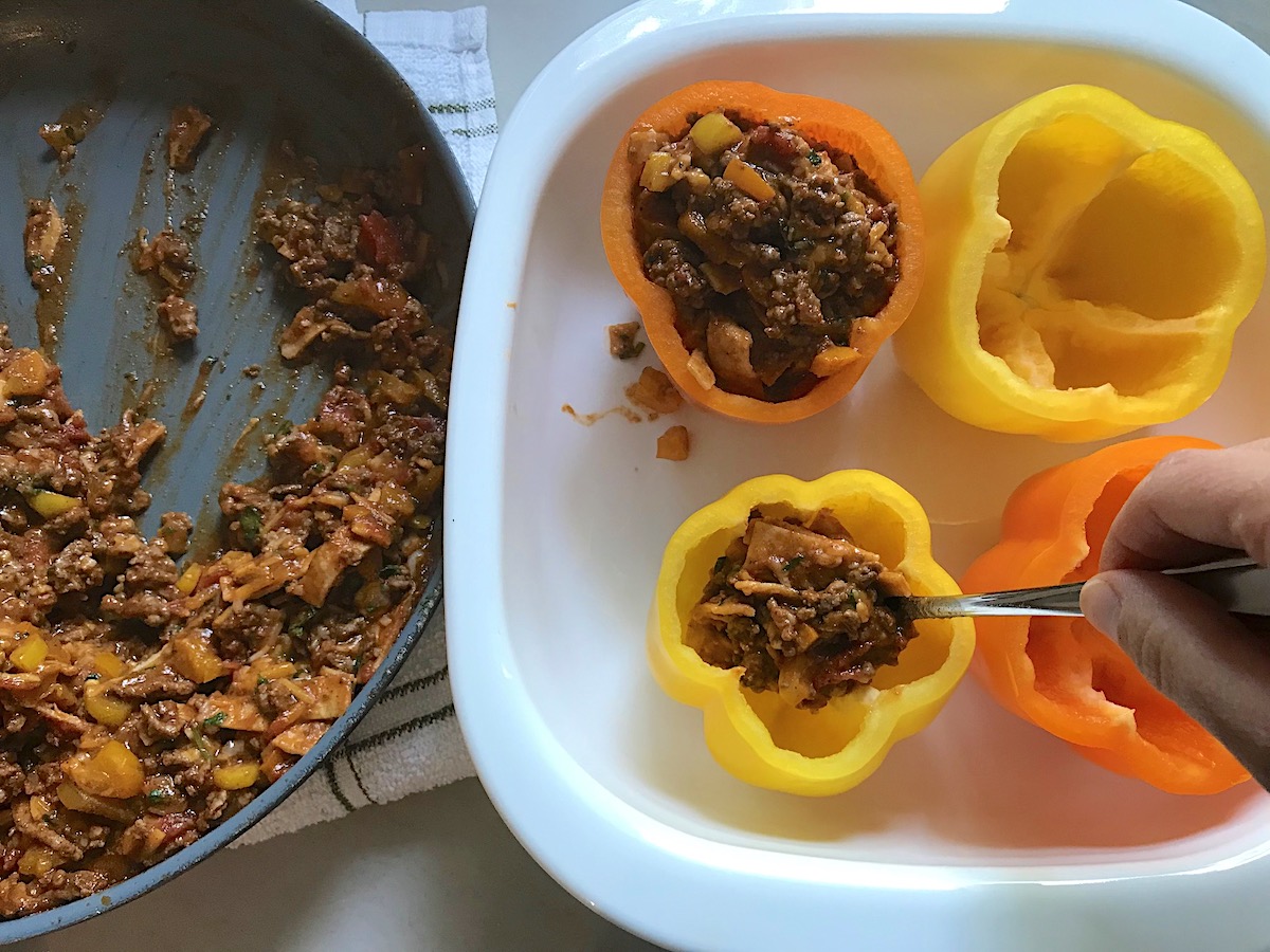 Hand filling yellow and orange bell peppers with Tex Mex beef filling for Stuffed Peppers without Rice.