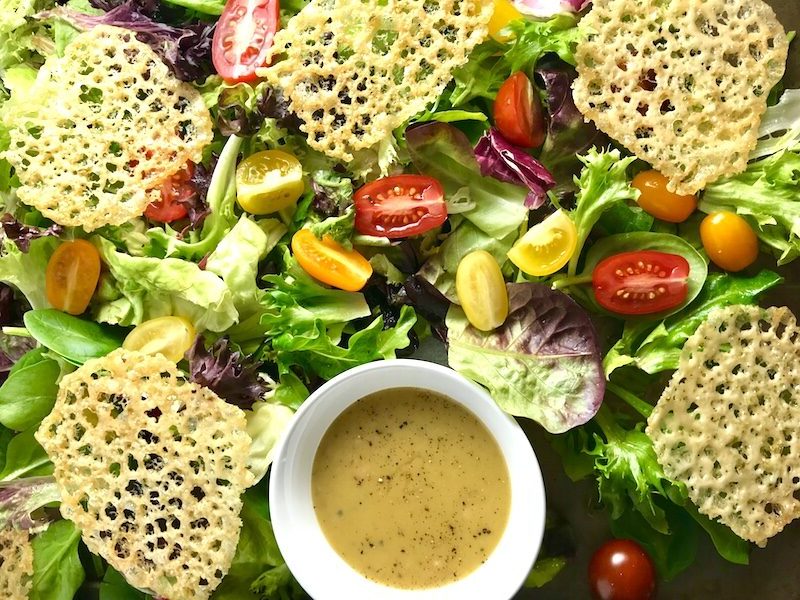 Salad on a platter with small bowl of vinaigrette and parmesan crips.