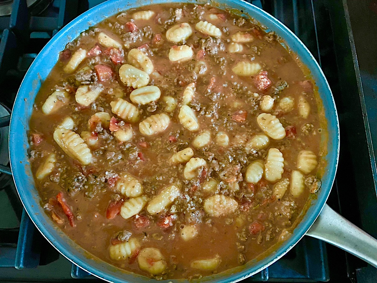 Ground beef sauce and gnocchi cooking in a skillet on the stove for Ground Beef Gnocchi skillet recipe.