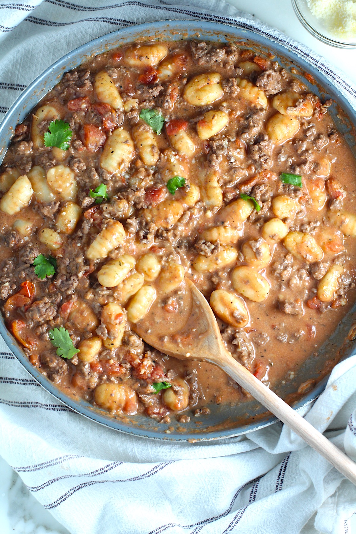 Ground Beef Gnocchi Skillet recipe on a plate with fresh parsley garnish in a skillet with a wood spatula.