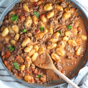Ground Beef Gnocchi Skillet recipe on a plate with fresh parsley garnish in a skillet with a wood spatula.