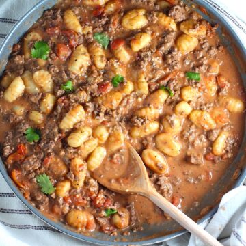 Ground Beef Gnocchi Skillet recipe on a plate with fresh parsley garnish in a skillet with a wood spatula.