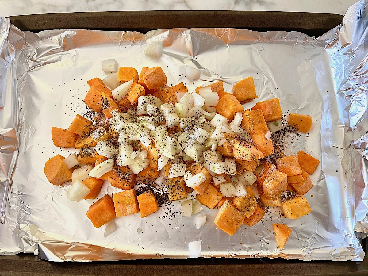 Butternut Squash cubed and diced onions on an aluminum foil lined sheet pan with seasonings before being combined and roasted for the Butternut Squash Spaghetti recipe.
