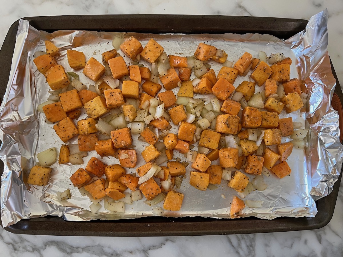 Butternut Squash cubes, diced onions, and seasonings combined on an aluminum foil lined sheet pan before being combined and roasted for the Butternut Squash Spaghetti recipe.