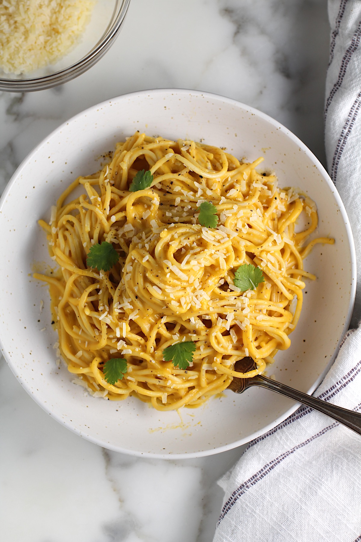 Creamy Butternut Squash Spaghetti on a plate on counter with fork and fresh parsley garnish on top.