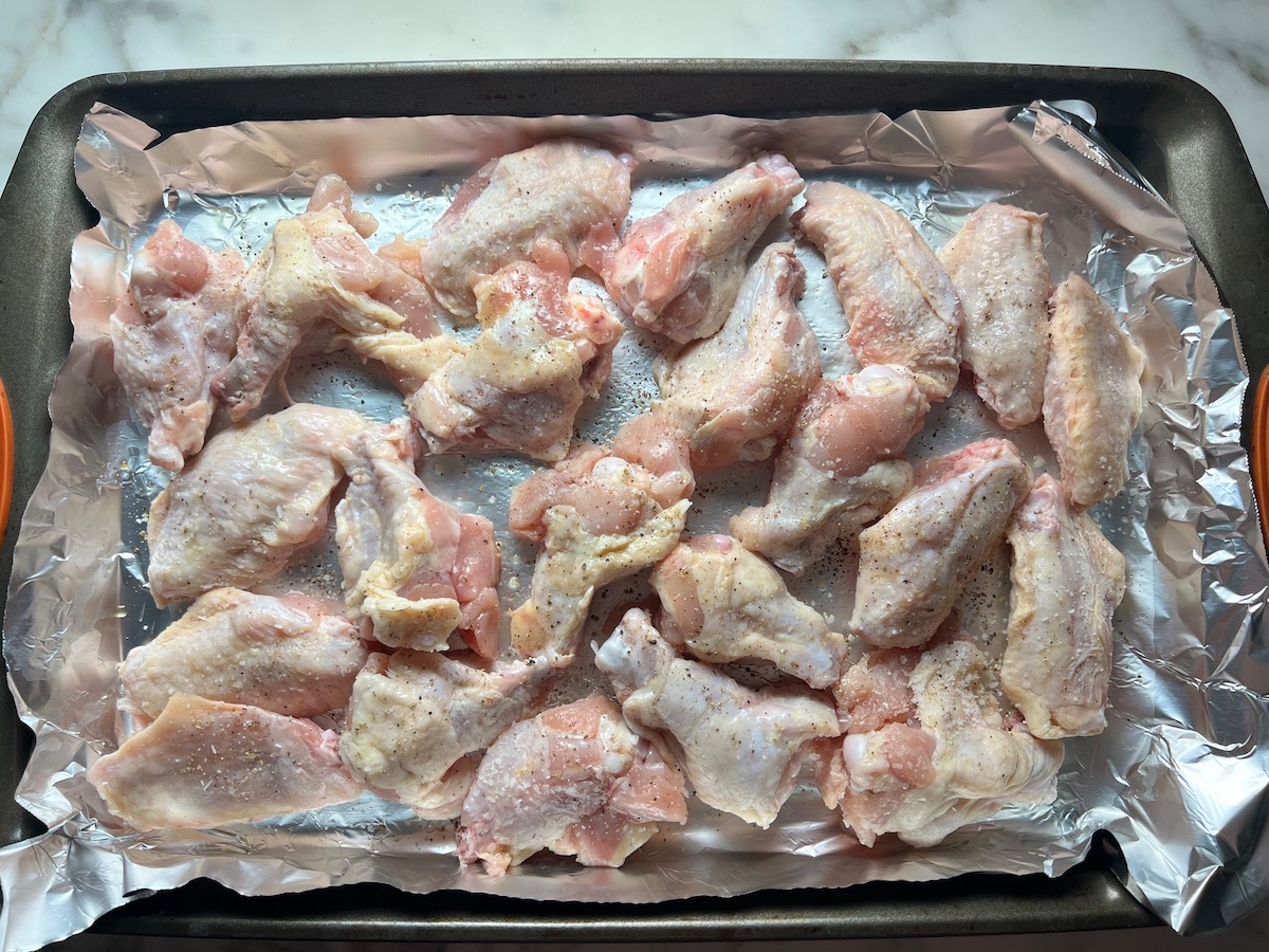 Raw seasoned chicken wings and drumettes on a foil-lined sheet pan for the Apricot Sauce Wings recipe.