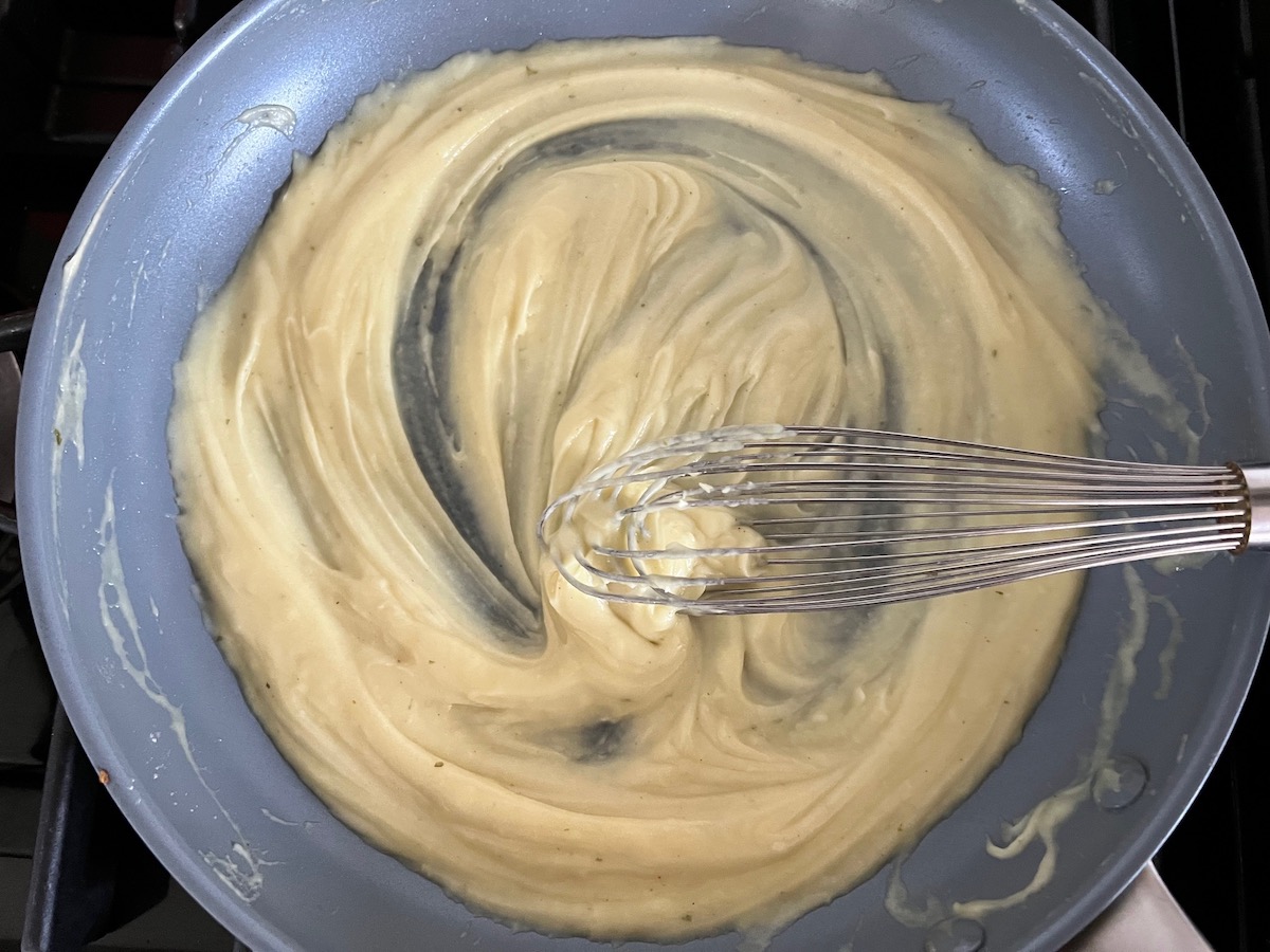 Broth being whisked into the flour and butter roux in a large frying pan on the stove for Mushroom Alfredo Fettuccine pasta.