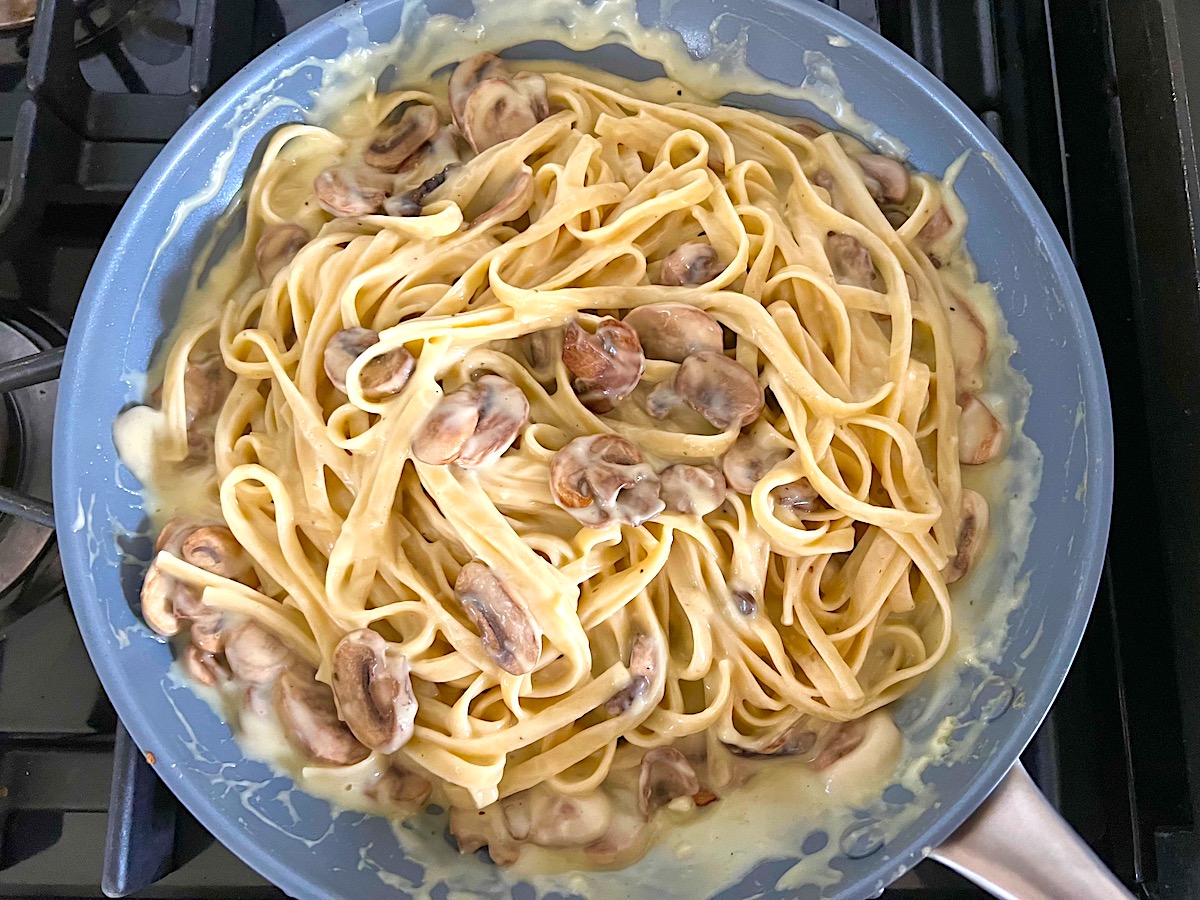 Mushroom Alfredo Fettuccine pasta in a pan with wooden tongs scooping up pasta.