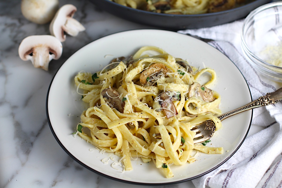 Mushroom Alfredo Fettuccine pasta on a plate with a fork with parsley sprinkled on top.