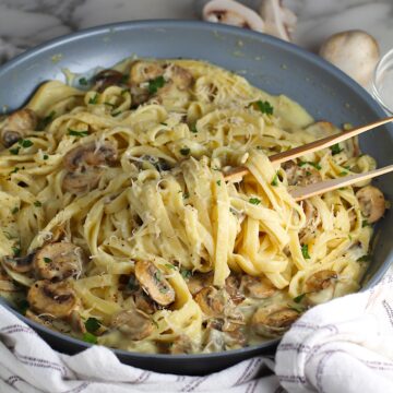 Mushroom Alfredo Fettuccine pasta in a pan with wooden tongs scooping up pasta.