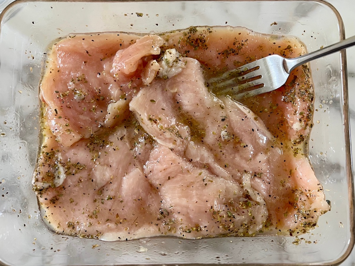 Raw chicken cutlets marinating in garlic, olive oil, oregano, salt, and pepper in glass dish for Chicken Ricotta Pasta Recipe.